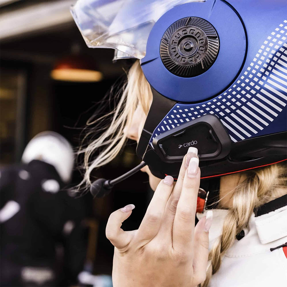 Blue CARDO Spirit HD helmet headset with black charging base held near rider
