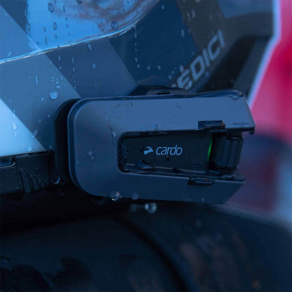Black intercom module mounted on a motorcycle helmet with green indicator