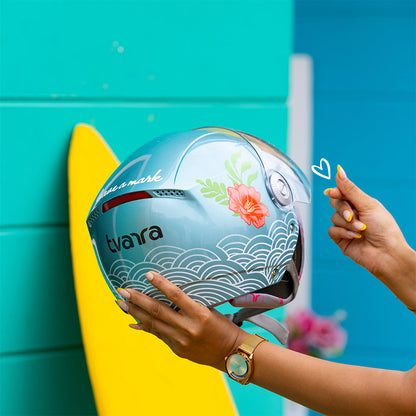Aqua blue motorcycle helmet held near a bright yellow board, wave graphic front